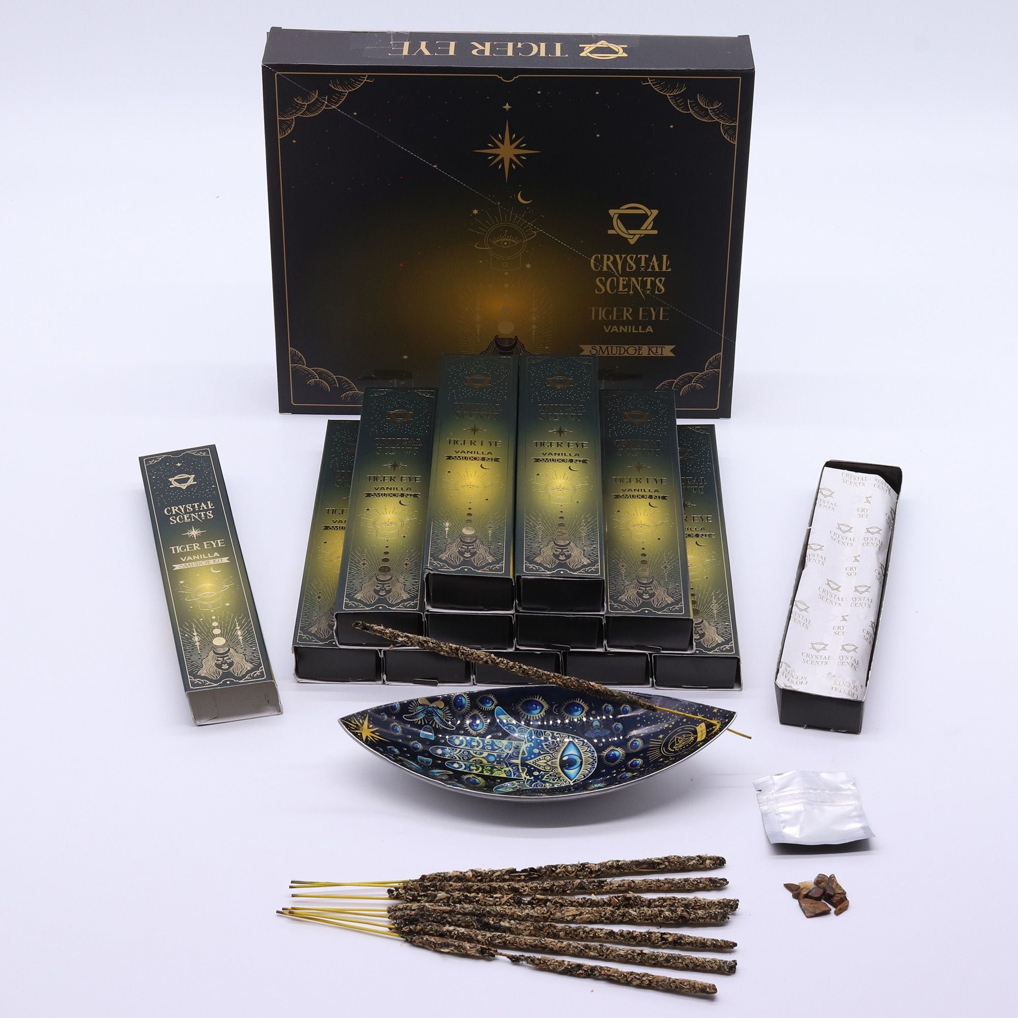 Encens Smudge Vanille accompagné d’éclats d’Œil de Tigre naturel. La boîte contient 10 bâtons d’environ 20 cm, fabriqués à la main en Inde et présentés dans un étui cartonné doré au style céleste.