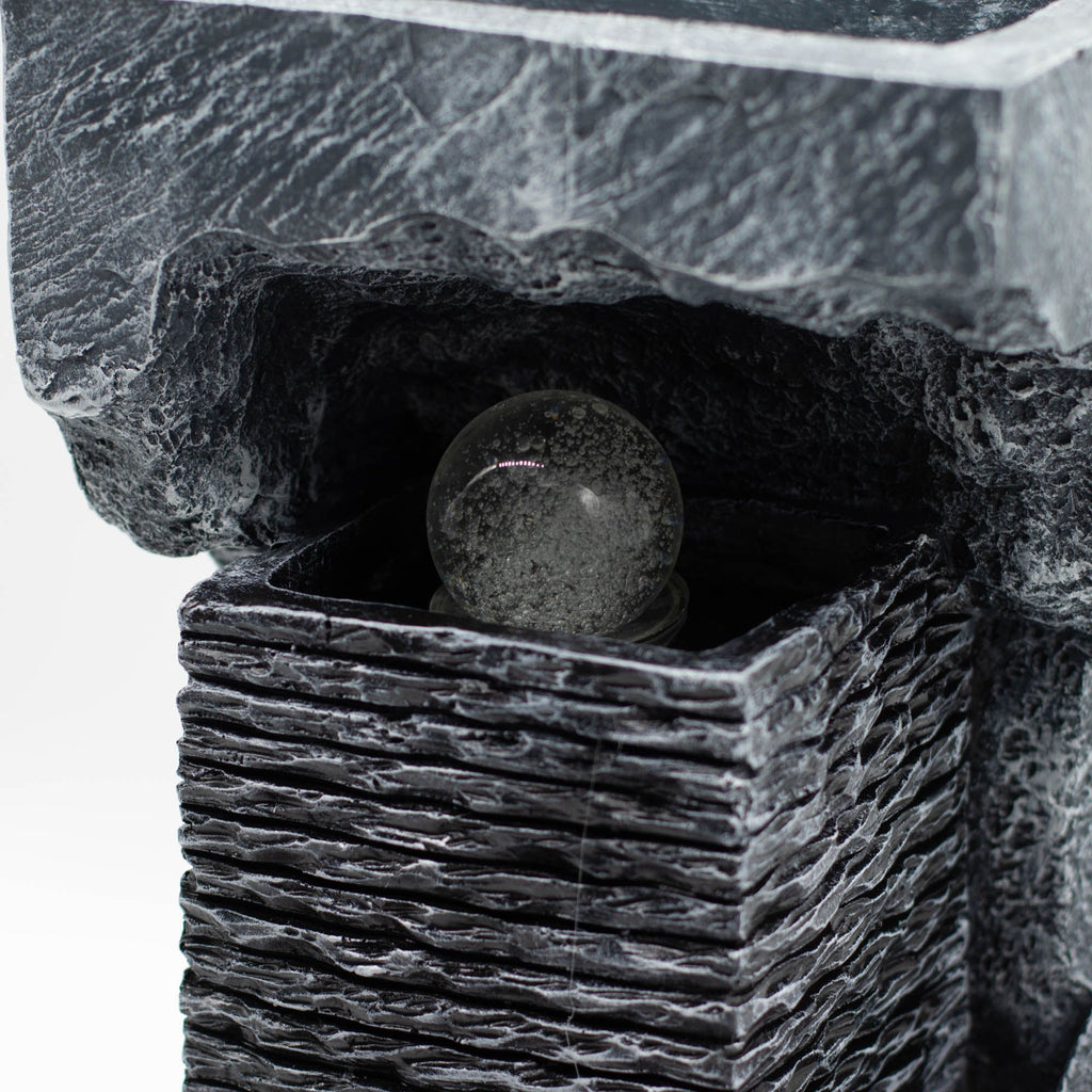 Gros plan d’une fontaine d’intérieur avec boule cristal, texture effet pierre et finitions sculptées.