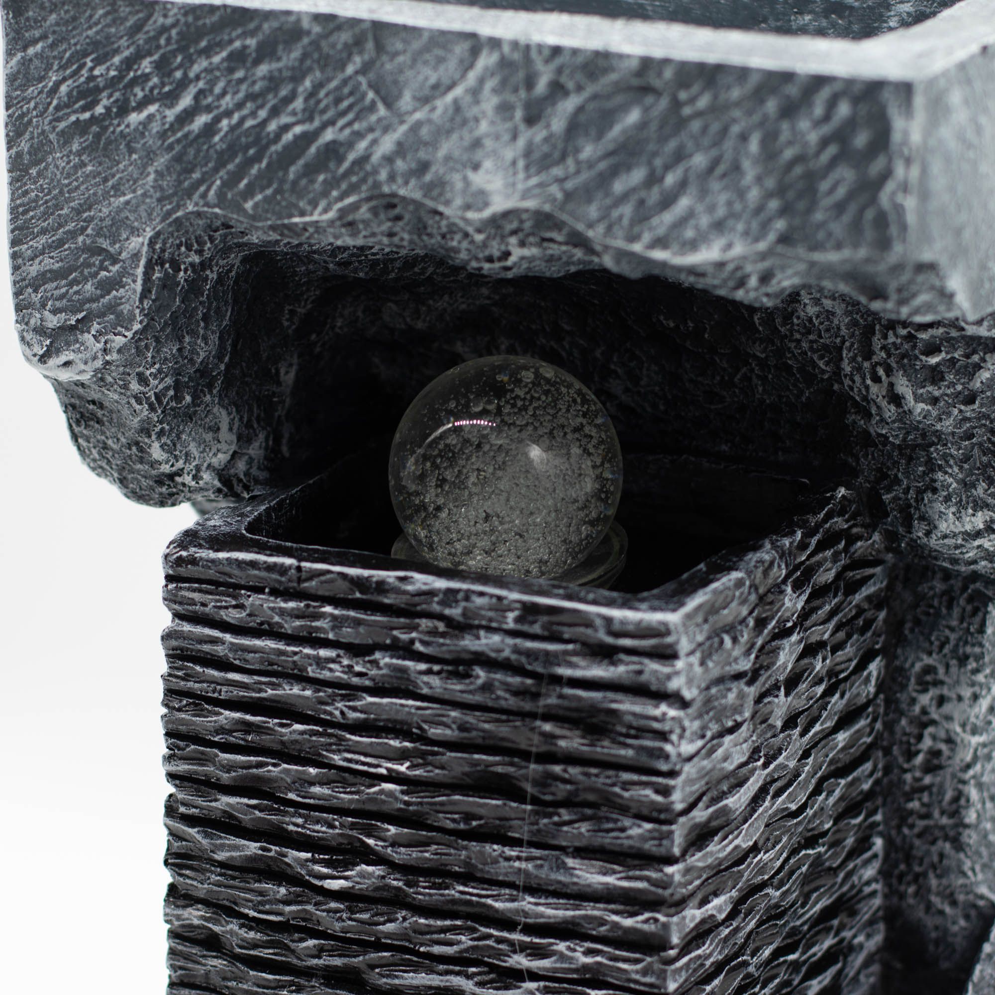 Gros plan d’une fontaine d’intérieur avec boule cristal, texture effet pierre et finitions sculptées.