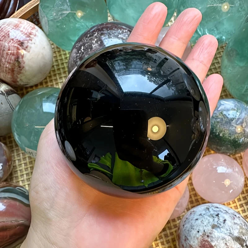 Sphère en obsidienne noire naturelle polie – de 2 à 13 cm sur un fond décoratif de minéraux, idéale pour enrichir votre espace avec une boule décorative minérale.