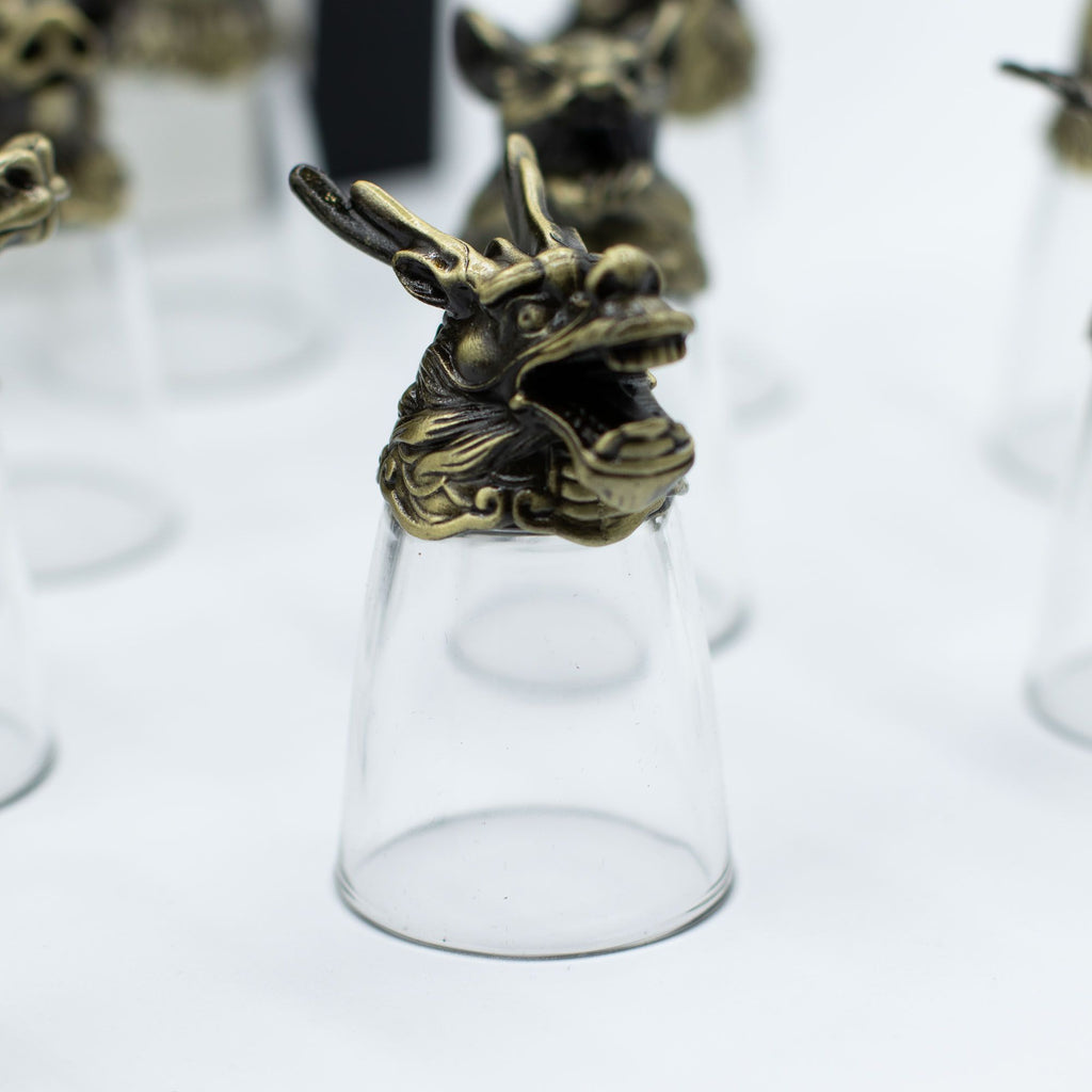 Focus sur un verre à shot en bronze antique, représentant un dragon dans le lot de 12 Bottom Up Shot Glasses (25ml). Parfait pour les amateurs de zodiaque chinois, ce verres à shot de 25 ml se distingue comme un accessoire de bar exceptionnel. Offrez ce coffret cadeau original qui allie culture et élégance, idéal pour les arts de la table.