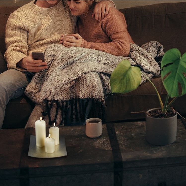 Un couple détendu sur un canapé, profitant de moments ensemble avec une ambiance crée par la Bougie Biplante Élégante 60x150mm - rouge.