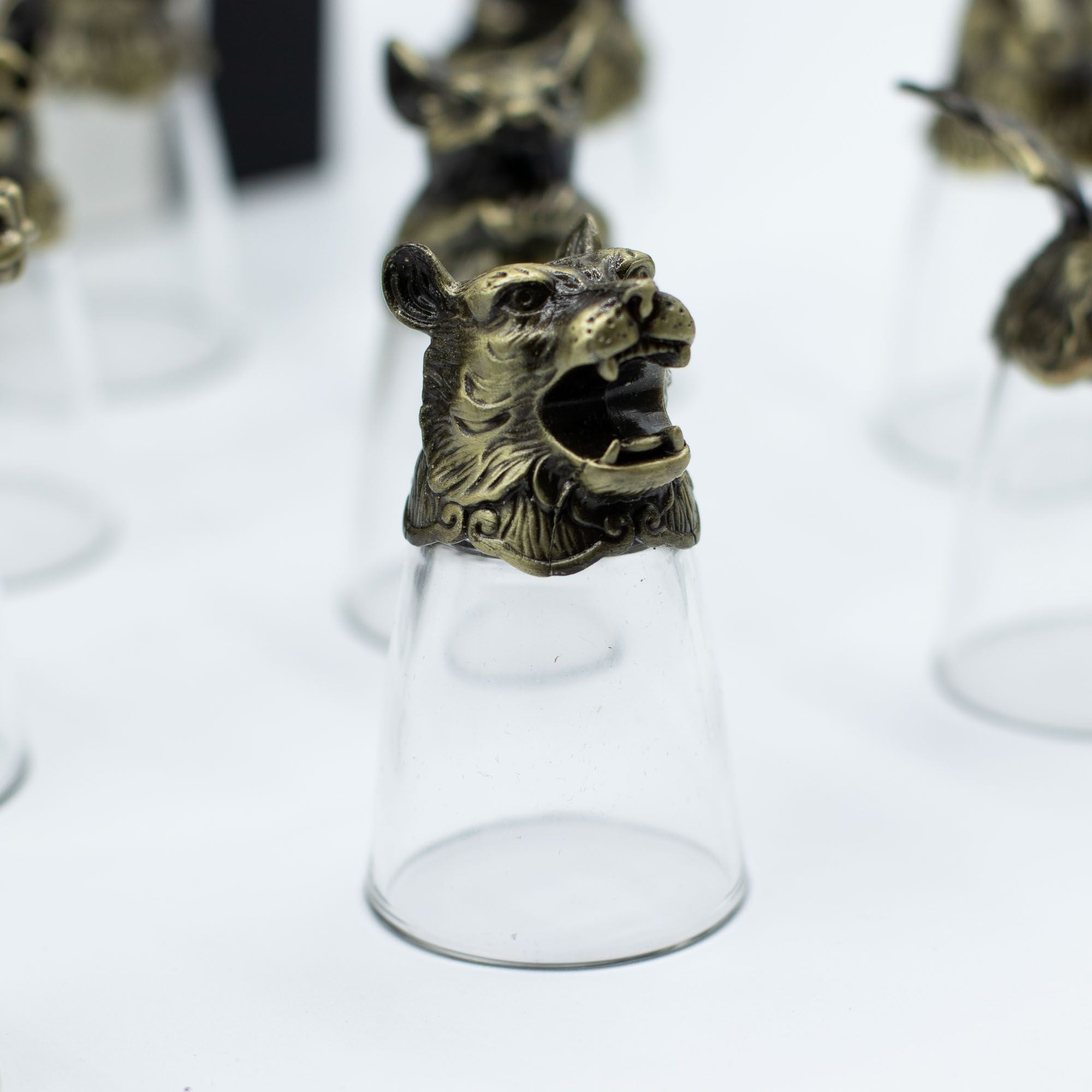 Détails d'un verre à shot en bronze antique dans l'ensemble des Bottom Up Shot Glasses (25ml) mettant en avant un lion. Ce lot de 12 verres à shot, idéal pour les accessoires de bar, incarne l'esprit des animaux du zodiaque chinois. En tant que cadeau original, ce coffret fait briller les arts de la table tout en offrant une touche unique. Aemilia Mystica.