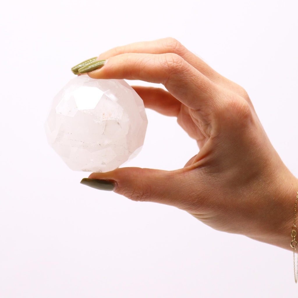 Boule De Guérison En Cristal De Roche tenue à la main, en cristal de roche facetté, un excellent outil pour la méditation et la lithothérapie, accompagnée d'un support en bois, parfaite pour apporter sérénité et décoration spirituelle, proposée par Aemilia Mystica.