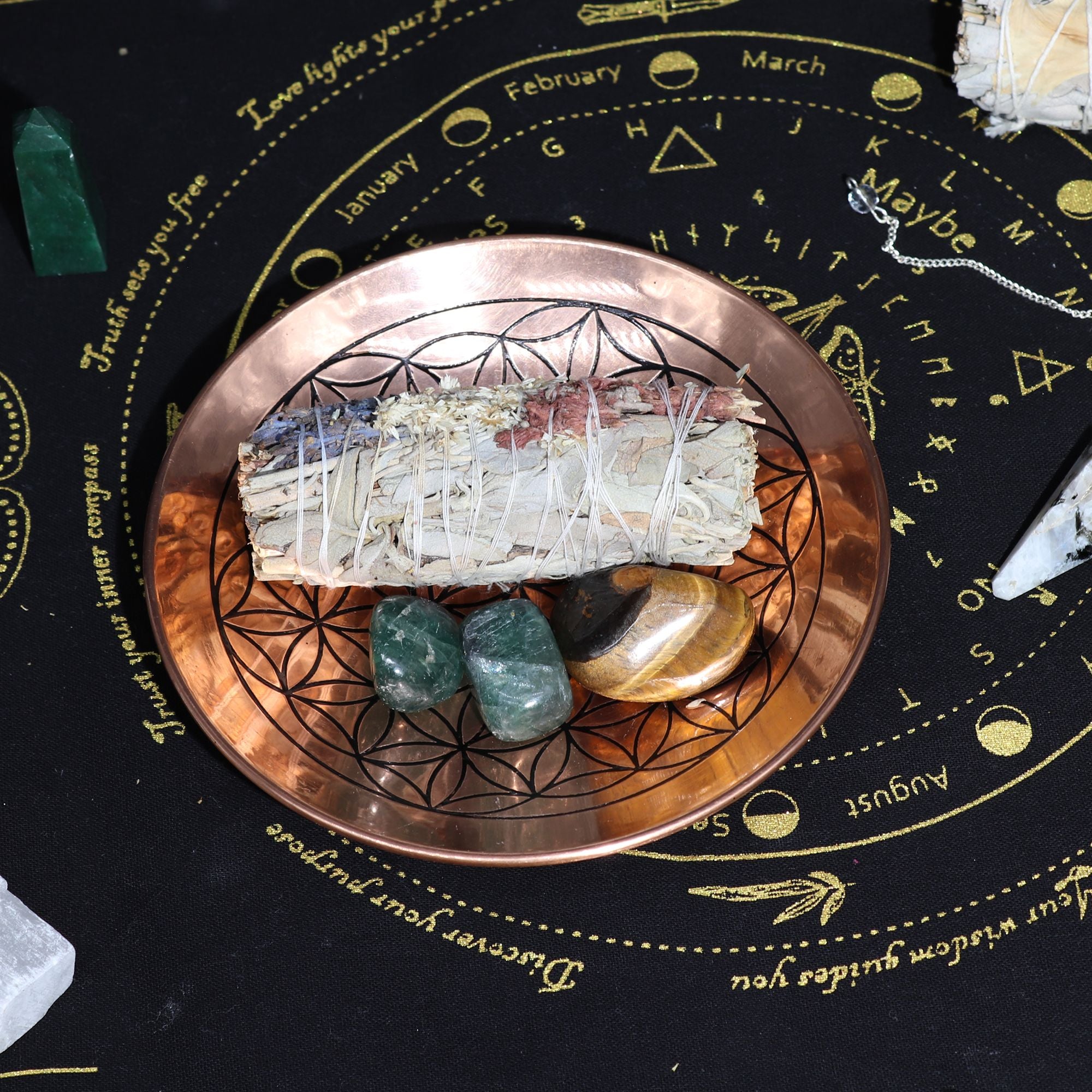 L'Assiette d’Offrande en Cuivre Fleur de Vie garnie d'herbes et de cristaux sur un tapis rituel. Cet accessoire d’autel est un objet ésotérique essentiel pour les pratiques de smudging, mixant esthétique et fonctionnalité dans vos rituels.
