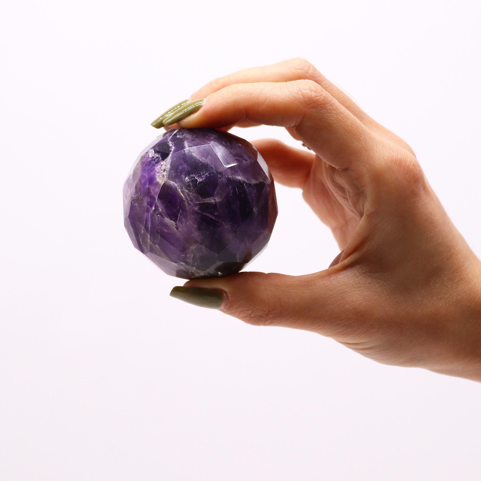 Boule De Guérison En Améthyste Facetée tenue dans une main, cette sphère améthyste fait ressortir la beauté de l'améthyste naturelle, spécialisée dans la lithothérapie. Utilisée pour la méditation, elle aide à développer la sérénité et l'intuition, tout en équilibrant le chakra couronne et le troisième œil. Un ajout parfait à votre décoration spirituelle de Aemilia Mystica.