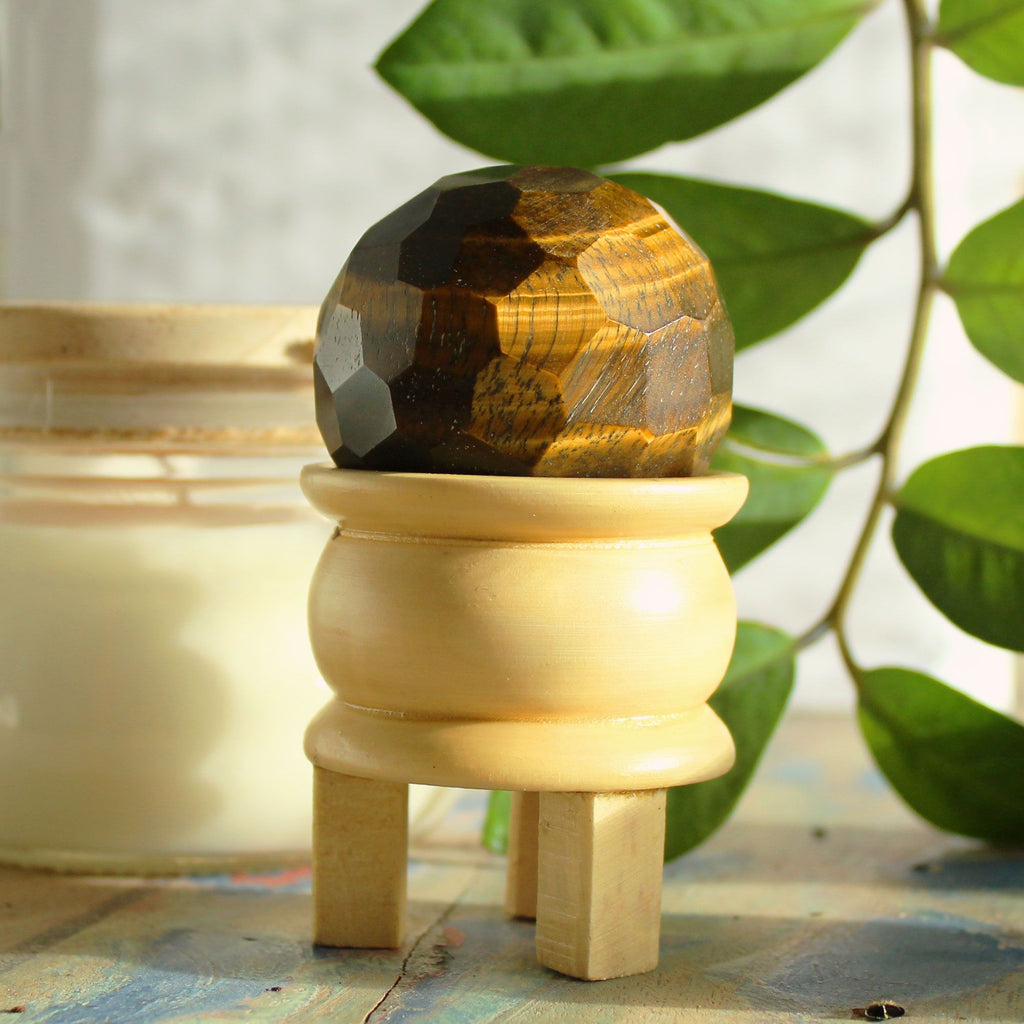 Gemstone Faceted Healing Ball & Stand - Tigereye. La boule oeil de tigre repose sur un élégant support en bois, ajoutant une touche de décoration spirituelle à votre espace. Cette sphère en pierre naturelle est parfaite pour l'ancrage et l'activation du chakra racine, offrant protection énergétique et confiance en soi.