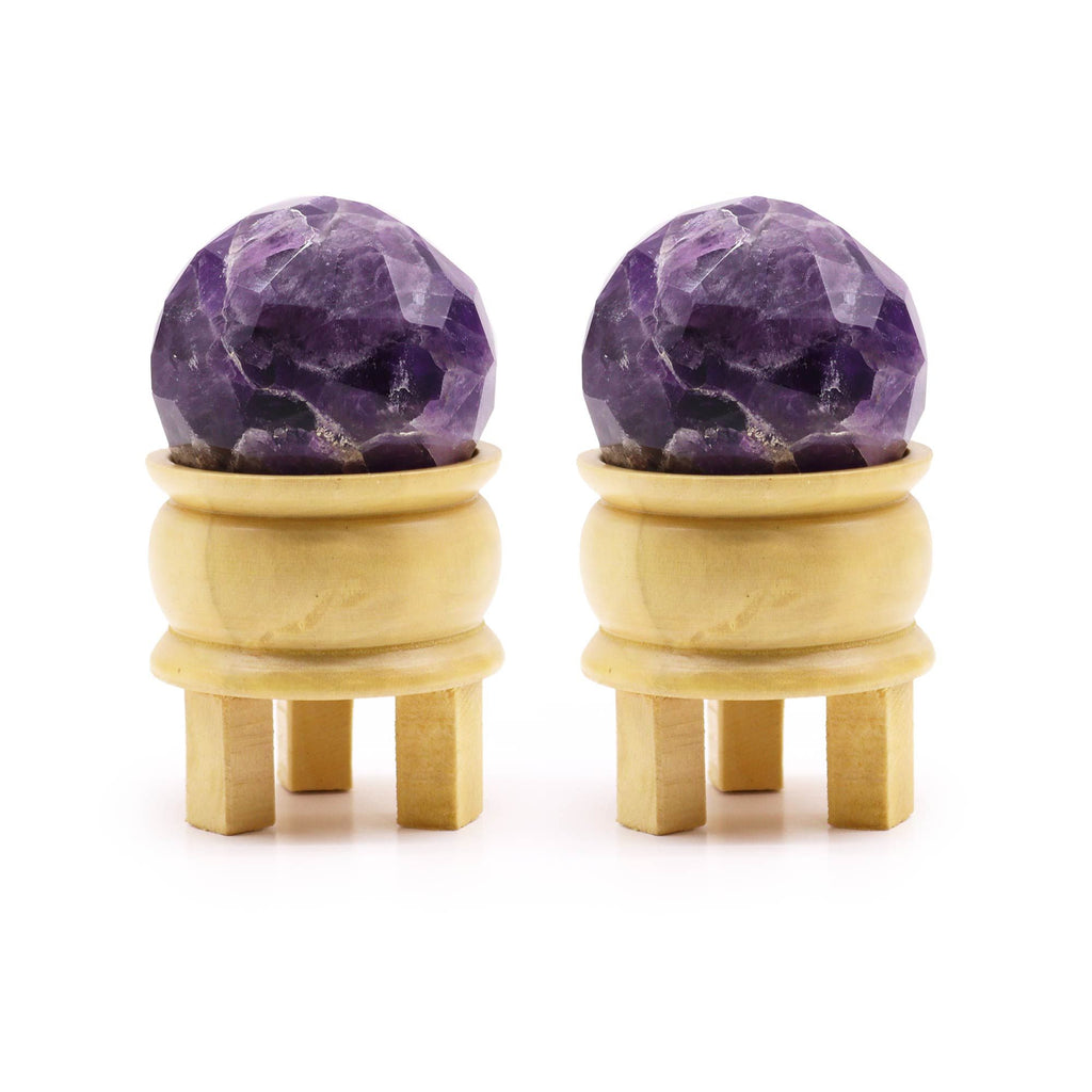 Boule De Guérison En Améthyste Facetée présentant deux sphères améthyste sur un support en bois. Ces boules en améthyste naturelle, facettées, sont idéales pour favoriser la sérénité et l'intuition dans la méditation. Parfaites en tant que pierres naturelles et cristaux naturels, elles apportent une touche de décoration spirituelle à votre environnement, représentant la marque Aemilia Mystica.