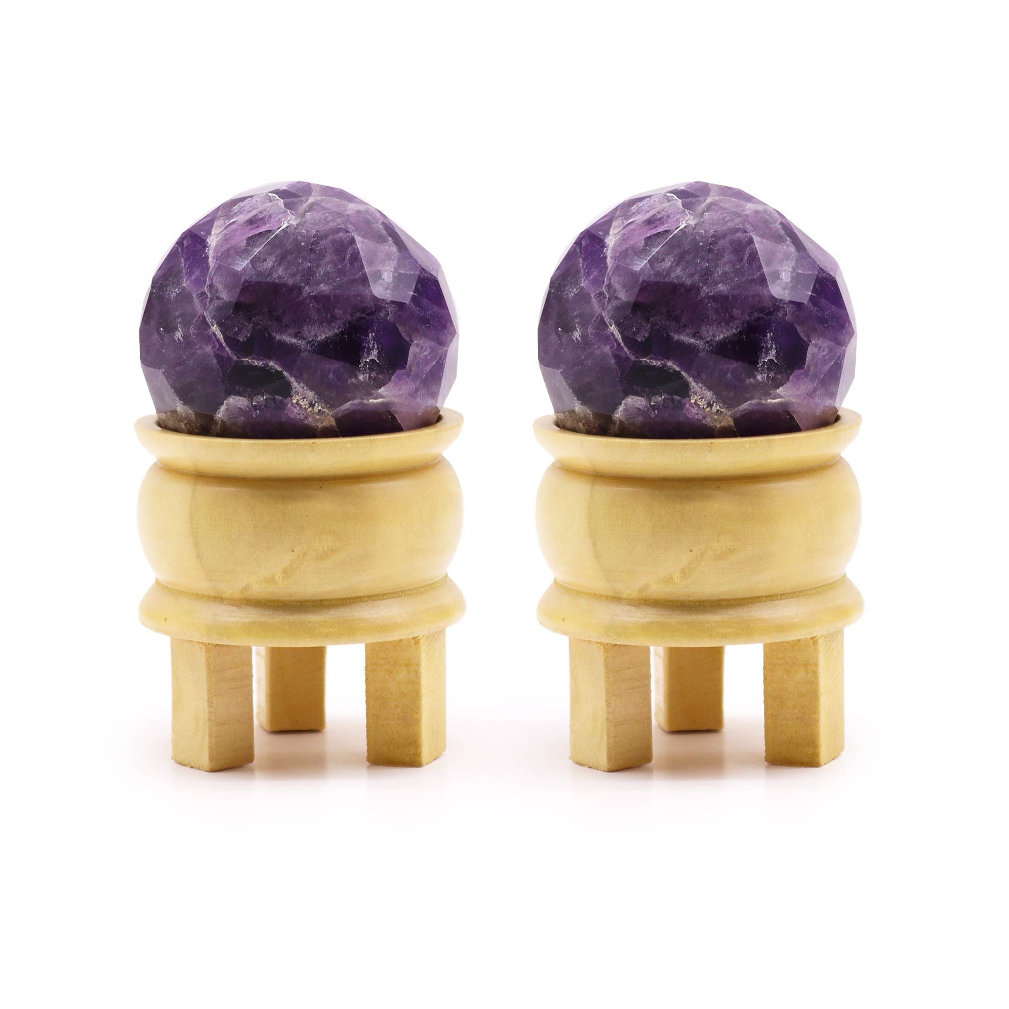 Boule De Guérison En Améthyste Facetée présentant deux sphères améthyste sur un support en bois. Ces boules en améthyste naturelle, facettées, sont idéales pour favoriser la sérénité et l'intuition dans la méditation. Parfaites en tant que pierres naturelles et cristaux naturels, elles apportent une touche de décoration spirituelle à votre environnement, représentant la marque Aemilia Mystica.