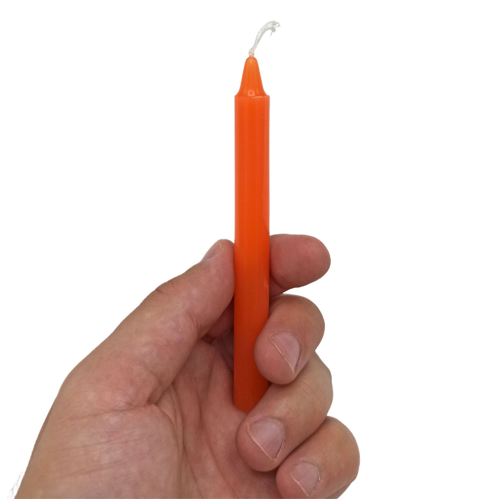 Une main tenant une bougie orange de la collection Bougies Manifest Magic (lot de 12) - Orange - Chakra sacré, idéale pour activer le chakra sacré et favoriser la créativité, l'expression émotionnelle et la méditation.