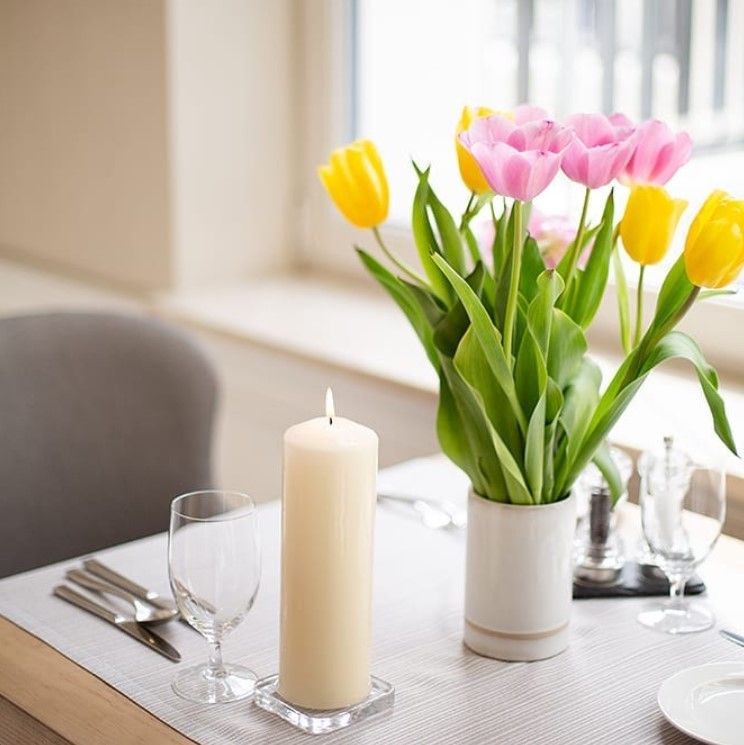 Table soigneusement dressée avec la Bougie Biplante Élégante 80x250mm - Ivoire et un vase de tulipes colorées, idéale pour les dîners raffinés.