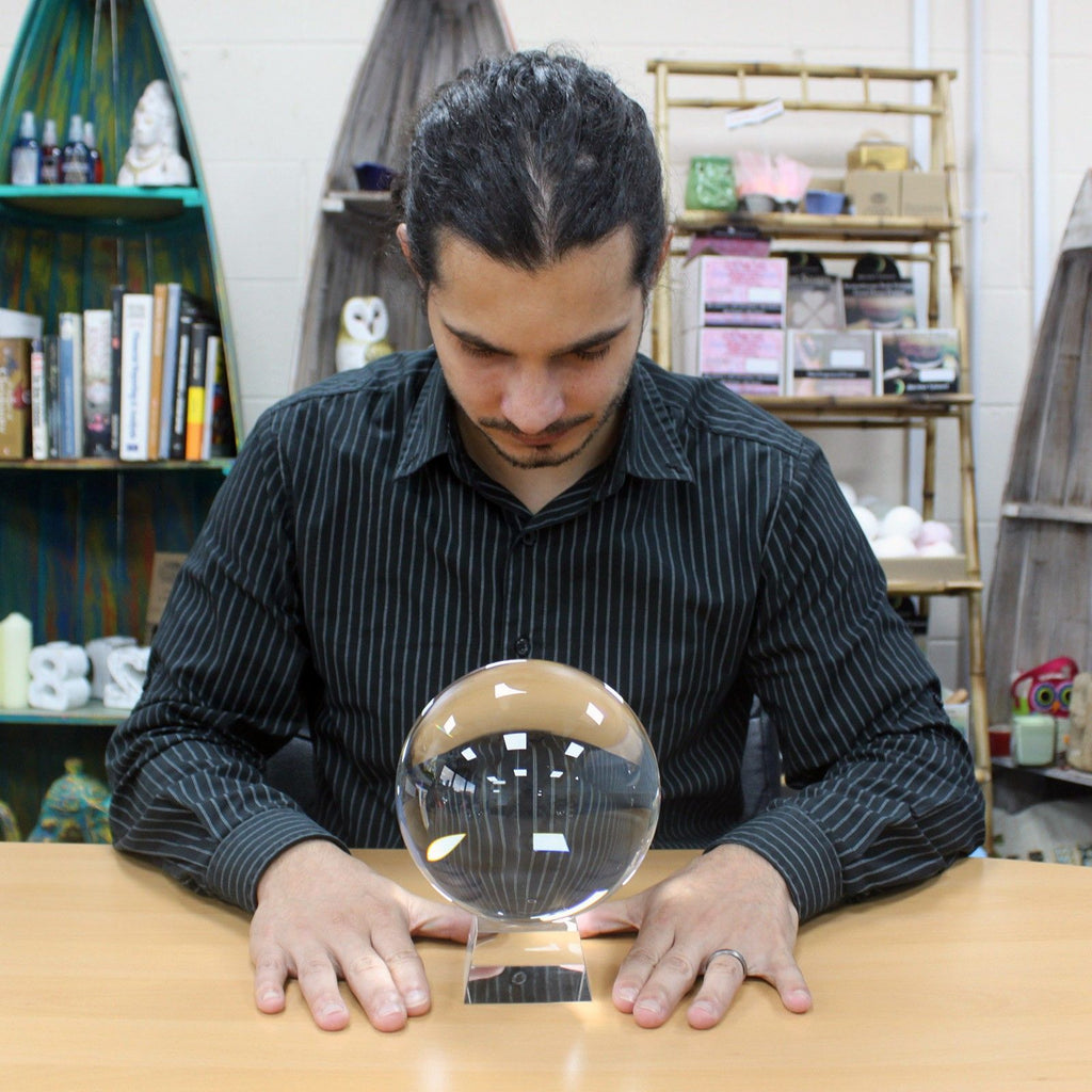 Homme concentré sur une Boule de Cristal sur support – 150 mm, un accessoire spirituel parfait pour un autel ésotérique. Cette boule de cristal 150 mm, symbolisant la divination, est une décoration mystique et spirituelle qui apporte une atmosphère ésotérique unique à tout espace.
