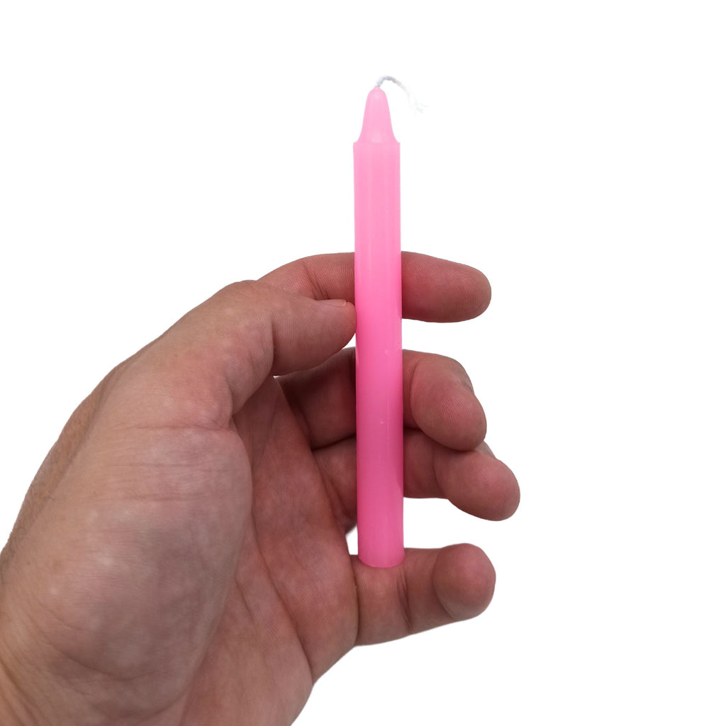 Bougies Manifest Magic (lot de 12) - rose - Déesse, illustrant une bougie rose tenue à la main. Ces bougies sont idéales pour les rituels méditatifs, apportant amour, beauté et sérénité tout en incarnant la grâce et la transformation liées à la Déesse.