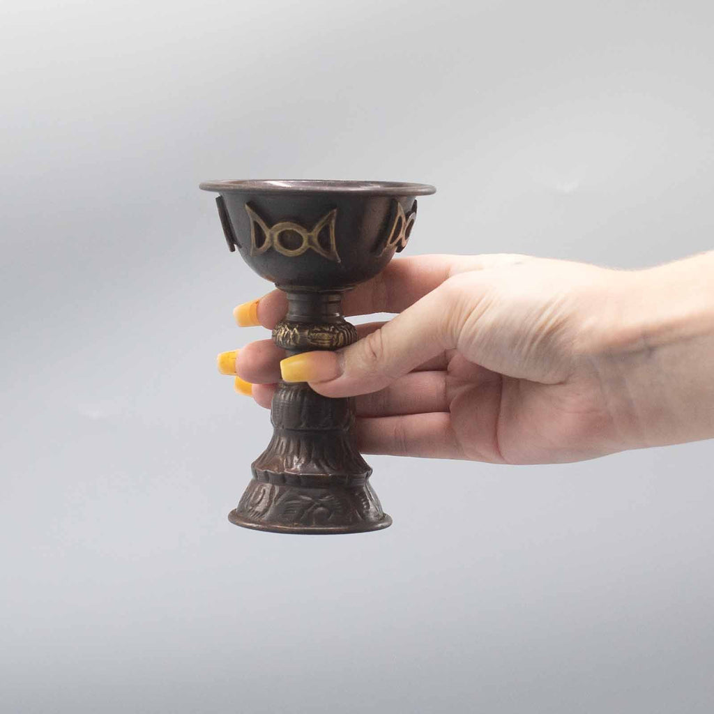 Calice Rituel en Cuivre Antique Triple Lune, tenu à la main, illustrant sa taille parfaite pour un usage personnel. Ce gobelet rituel est une pièce essentielle pour vos cérémonies spirituelles, vous accompagnant dans vos offrandes. Parfait comme accessoire rituel, il incarne le féminin sacré et la magie moderne à travers son design en cuivre antique.
