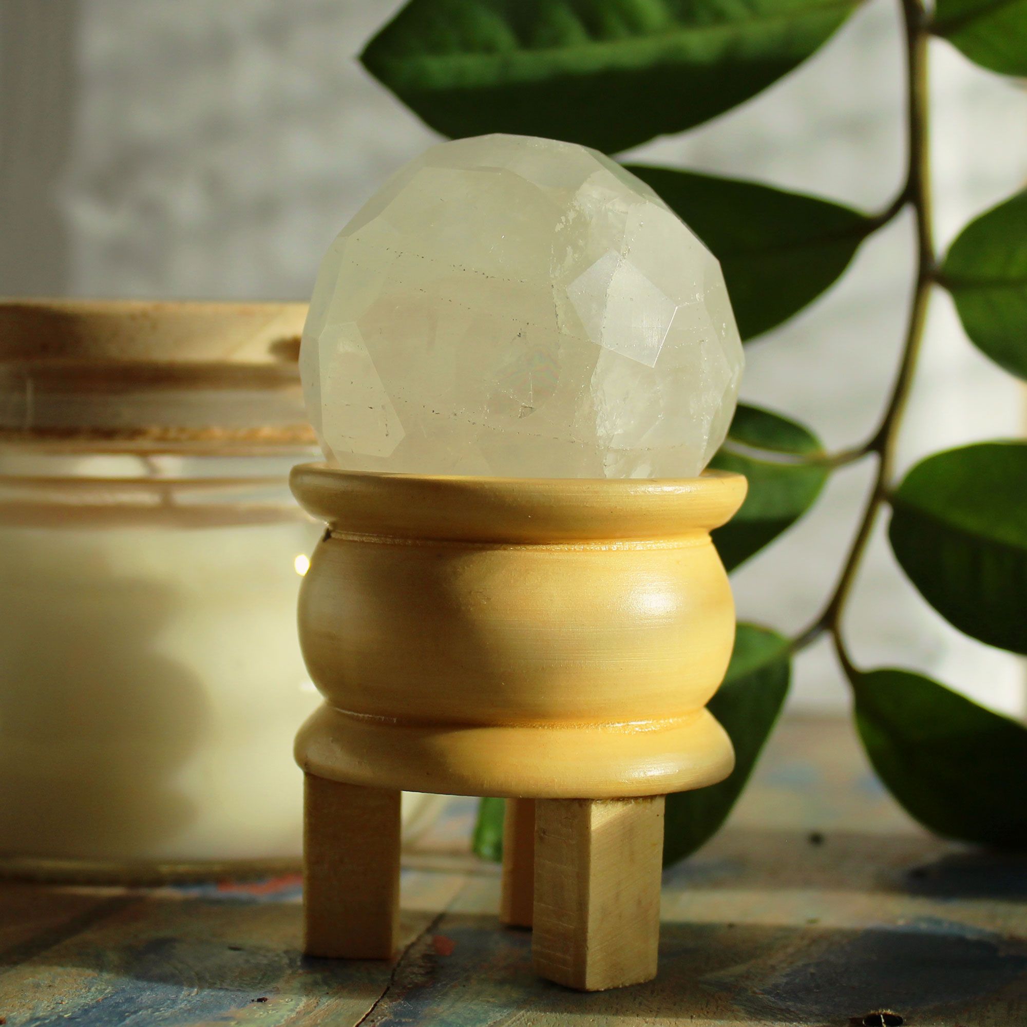 Boule De Guérison En Cristal De Roche avec un support en bois, mettant en avant la beauté du cristal de roche naturel et facetté, adaptée à la purification énergétique et à l'harmonisation énergétique, idéale pour votre espace méditatif de Aemilia Mystica.