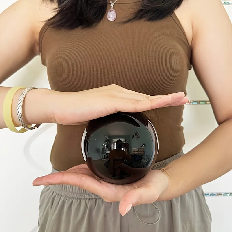 Grande boule en obsidienne noire naturelle polie tenue entre les mains pour montrer son format